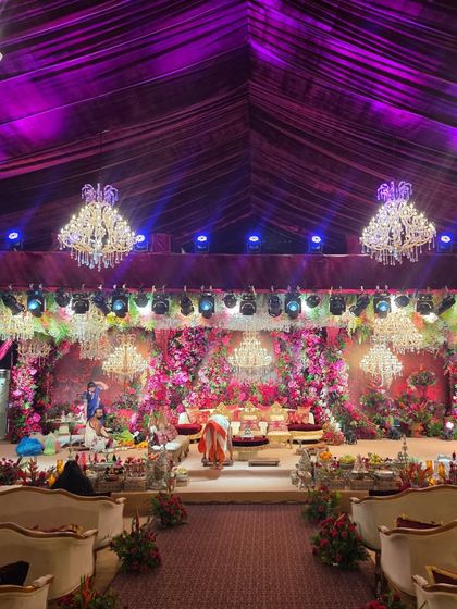 A full view of the grand floral wedding stage and the guest seating area. The purple uplighting and extensive floral work create a cohesive and luxurious ambiance throughout the venue.