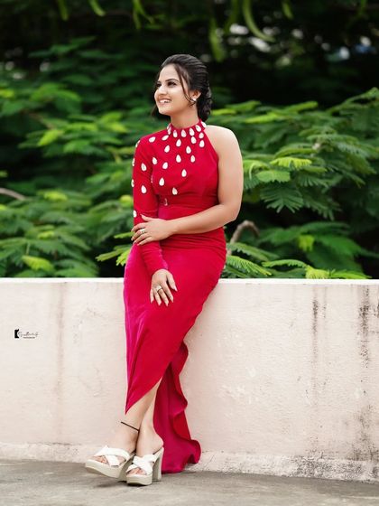 A full-length shot of Thanvi in her striking red gown. The makeup and hair are styled to create a complete, high-fashion look.