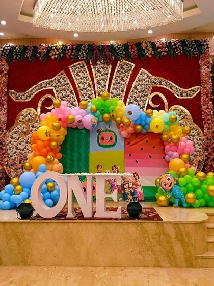 A grand stage setup for a Cocomelon first birthday party. This design uses a large 'ONE' prop, a vibrant balloon arch, and character cutouts on a fully decorated stage.