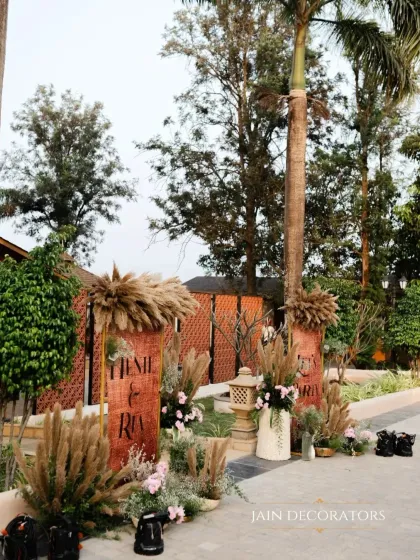 A rustic and chic entrance detail. The welcome sign is framed by arrangements of pampas grass and soft pink flowers, setting a warm and inviting tone.
