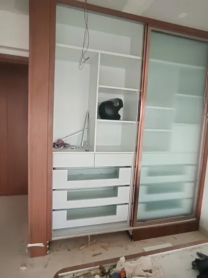 A wardrobe under construction, showing the internal drawer system and shelving before the fluted glass doors are installed.