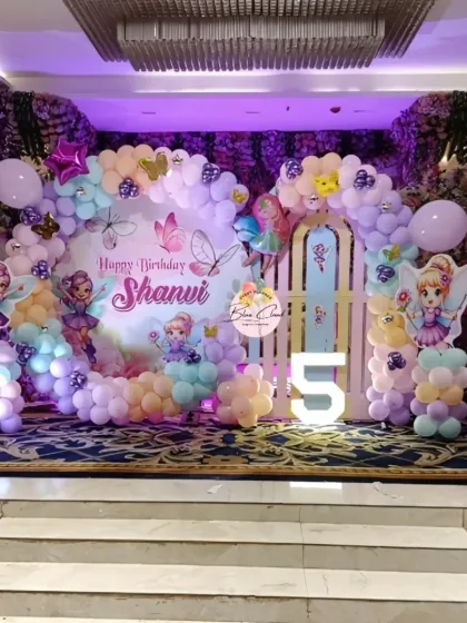 We created this enchanting fairy garden for a 5th birthday celebration. The stage decoration includes a custom backdrop with fairy illustrations, pastel balloon arrangements, and a large light-up number '5'.