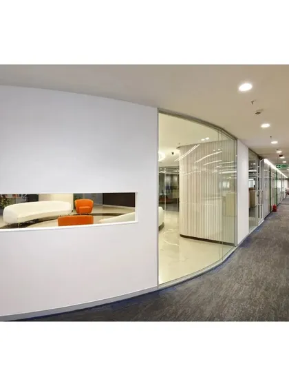 A curved glass wall and a unique wall cutout provide a glimpse into a lounge area from the main office corridor. This architectural feature creates visual connection and depth between different functional zones.