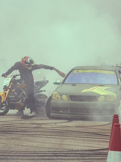 The same burnout shot from a different angle, capturing the raw energy and the partnership between car and bike performers.