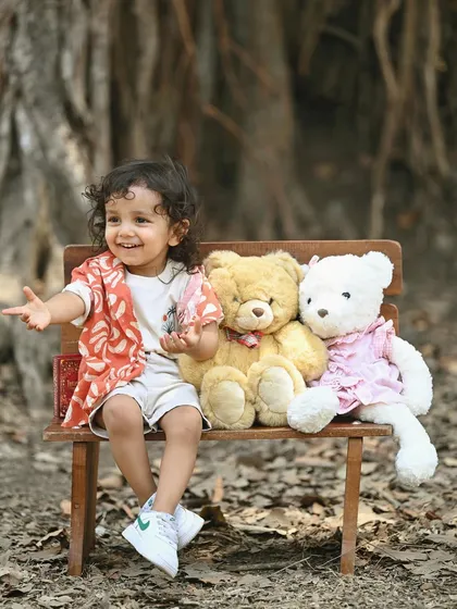 A sweet outdoor portrait of a little boy sitting on a bench with his teddy bear friends.