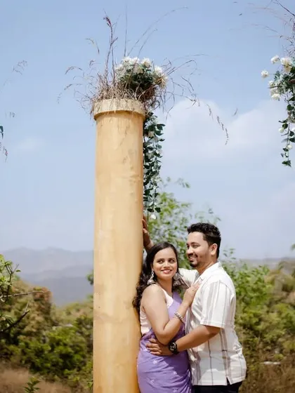 A wide shot showcasing the beautiful, rustic setting of the pre-wedding shoot, with the couple framed by decorated pillars.