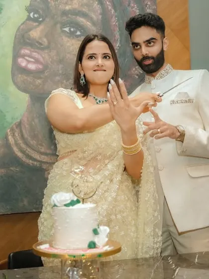 A joyous cake-cutting moment during an indoor engagement celebration in Pune. The couple's happiness is the focus, framed by modern decor and a beautiful piece of art, capturing the celebratory spirit of the occasion.