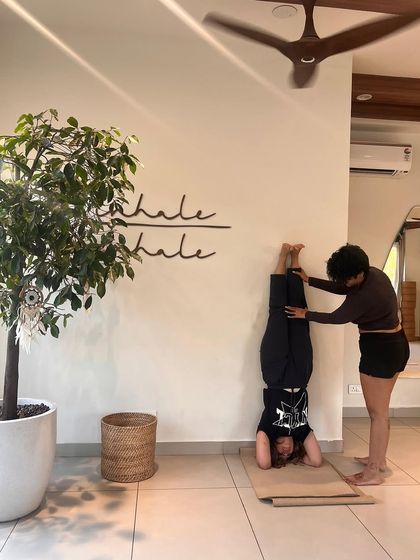 An instructor assists a student with a wall-supported headstand, demonstrating our commitment to helping students progress safely.