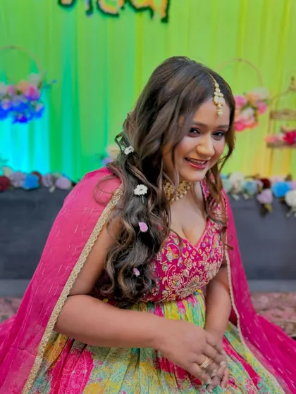 A happy Mehendi bride. Her hair is styled in soft waves with floral accents, and her makeup is a perfect balance of color and glow.