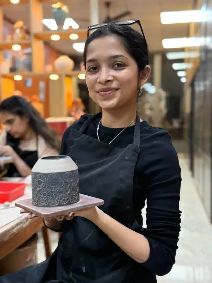 A student proudly shows off her finished sgraffito vase, featuring an intricate, hand-carved mandala pattern. In our classes, you will learn detailed decoration techniques to make your pottery truly one of a kind.