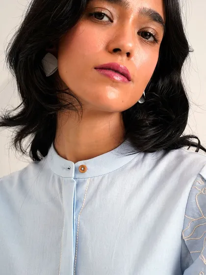 A close-up of the light blue shirt, showing the delicate embroidery on the sheer puff sleeves.
