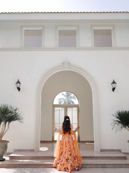 The bride, seen from the back, walking towards the entrance of a beautiful white villa for her Haldi ceremony. This shot builds a sense of anticipation.