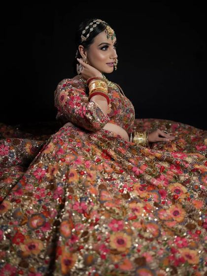 This image captures a dramatic bridal portrait. The hair is styled in a sleek updo to support the matha patti, ensuring the focus remains on the model's expressive features and the stunning floral lehenga.