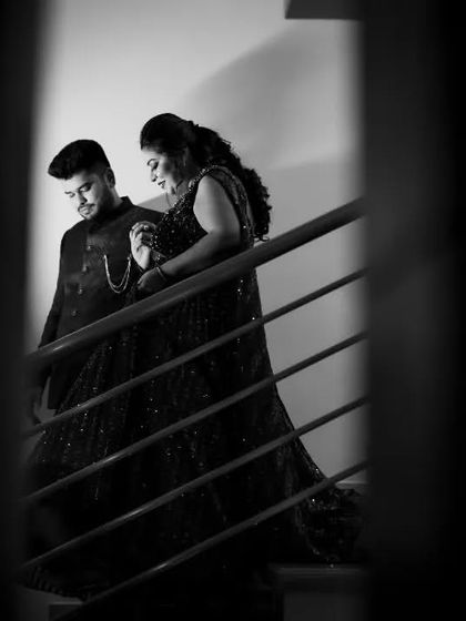 A dramatic black and white photo of a couple on a staircase during their Sangeet night, framed through railings for an artistic effect.