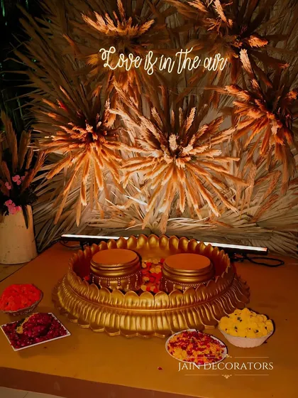 The Haldi ceremony essentials, beautifully presented. The golden platter and bowls are set against a backdrop of pampas grass, blending rustic textures with traditional elements.