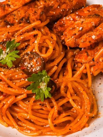 A close-up of arrabbiata spaghetti topped with slices of grilled chicken. The tight framing and moody lighting create a dramatic and highly appetizing image.