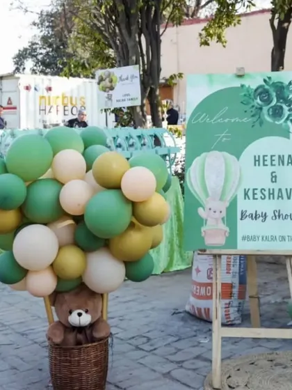 A teddy bear in a wicker basket with a bunch of balloons creates a whimsical hot air balloon prop, perfect for a baby shower welcome area.