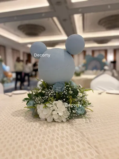 A close-up of a beautiful table centerpiece featuring a Mickey Mouse silhouette made of foam, nestled in a bed of white and blue flowers.