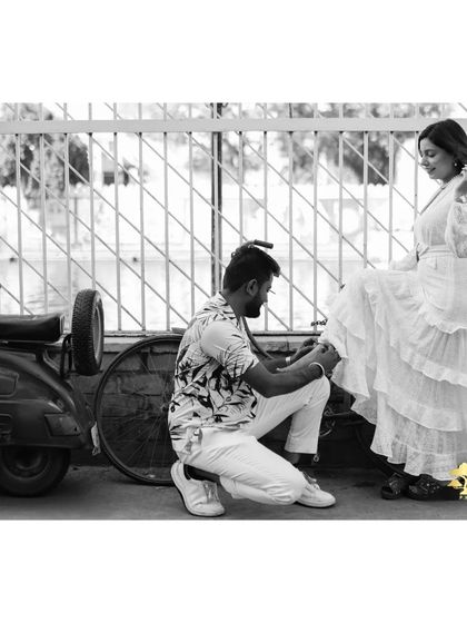 A sweet, candid moment captured in black and white. The groom helping the bride with her shoe by a vintage scooter feels like a scene from a classic movie.