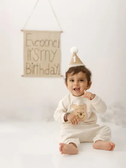 A happy little boy in his Winnie the Pooh outfit, celebrating his first birthday in our minimalist studio setup.