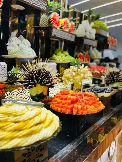 A close-up of the fruit selection, showing sliced pineapple, papaya, and artistically carved watermelon.