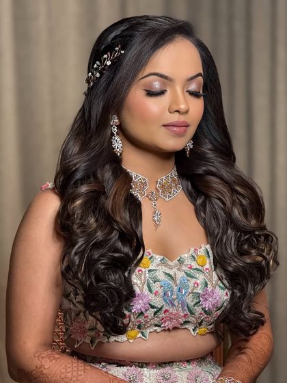 A soft and romantic look for a Sangeet or reception. The bride is wearing a floral embroidered lehenga with her hair in soft waves, and the makeup is glowing and ethereal.
