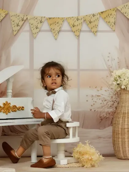 A toddler looks curiously to the side while sitting at a miniature piano, creating a thoughtful and artistic portrait.