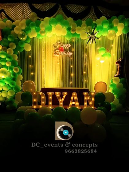 This birthday decor features a vibrant green and yellow balloon arch, a backlit curtain, and large, illuminated marquee letters spelling out the birthday boy's name.