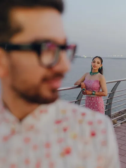 A creative portrait using foreground blur to create a sense of intimacy. The focus is on the bride looking out over the water, with the groom as a soft presence in the frame, suggesting his perspective.