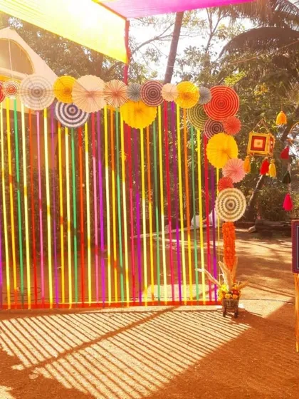 A fun and quirky photo booth for a Haldi or Mehendi. The backdrop of colorful ribbons and paper fans, along with playful props, creates a perfect spot for fun pictures.
