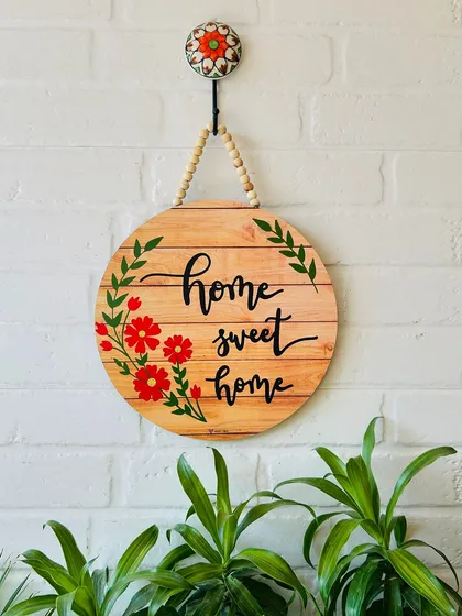 A beautiful 'Home Sweet Home' wooden sign, hand-doodled with red flowers. This 12-inch round sign is hung with jute twine and wooden beads, adding a rustic and personal touch to your entrance.