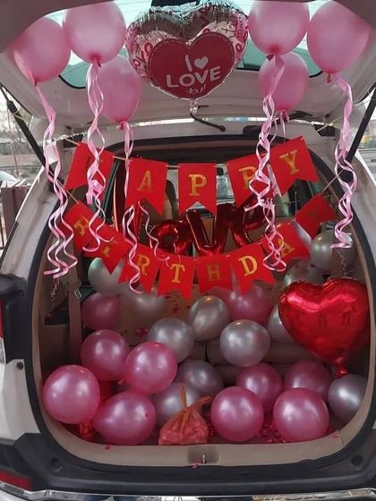 A romantic pink and silver themed car boot decoration. This birthday surprise is filled with balloons and includes a 'Happy Birthday' banner and 'I Love You' heart-shaped foil balloons.