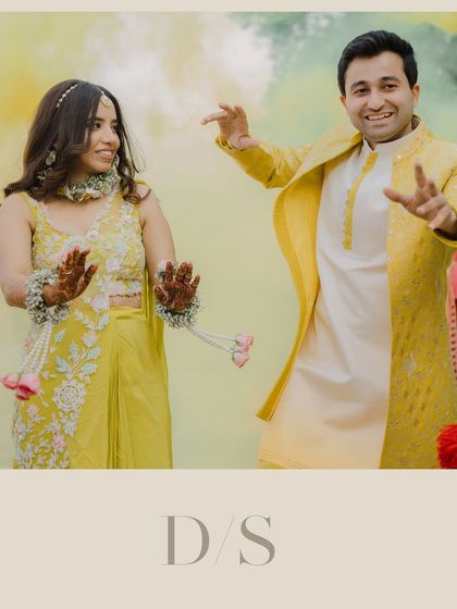A playful moment from the Haldi ceremony. The couple is seen dancing and enjoying the celebration, with colorful smoke in the background adding to the festive atmosphere.