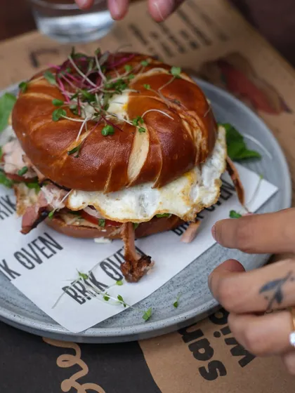 We're more than just pizza. This is our signature pretzel bagel sandwich, loaded with smoked ham, a perfectly fried egg, and fresh greens, served on our house-made bread.