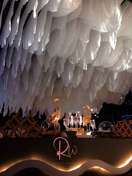A modern bar setup with a unique, cloud-like ceiling installation made of white fabric. The golden flamingo figurines add a touch of playful luxury.