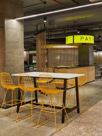 Another view of the high-top table, showing the "PAY HERE" sign in the background. The design uses a mix of materials including concrete, wood, and metal.