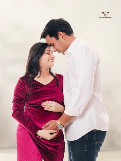 An intimate couple's portrait in the studio. They stand forehead-to-forehead, sharing a quiet moment of connection, with the mother-to-be in a rich velvet magenta dress.