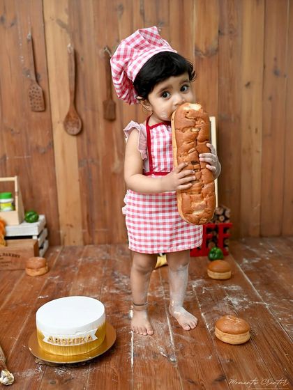 A big bite of bread for our little baker. This candid moment during her chef-themed cake smash shows her playful and curious personality.