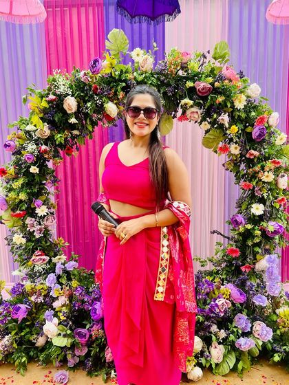Posing with my mic before a Haldi ceremony begins. The beautiful floral arch set the perfect backdrop.