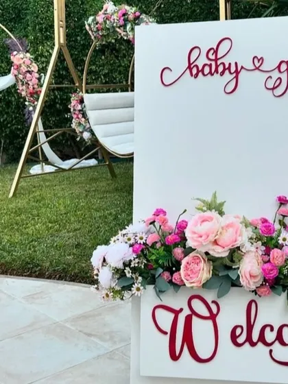 A beautiful floral welcome sign for the baby girl's party, featuring custom red lettering and a base of fresh pink and white flowers.