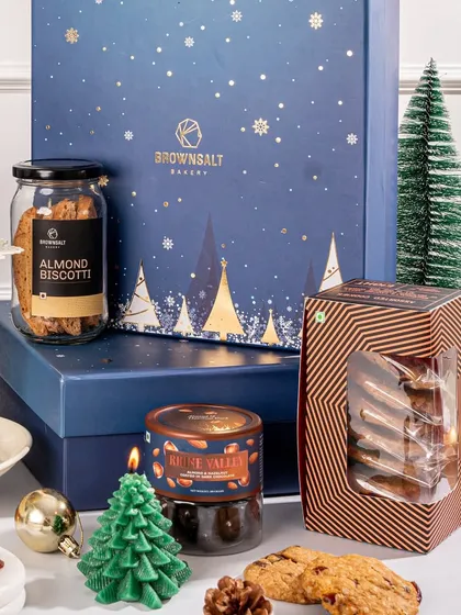 A detailed look at the contents of a Christmas gift box. You can see the almond biscotti, assorted cookies, a festive candle, and other treats, all carefully arranged for a beautiful presentation.