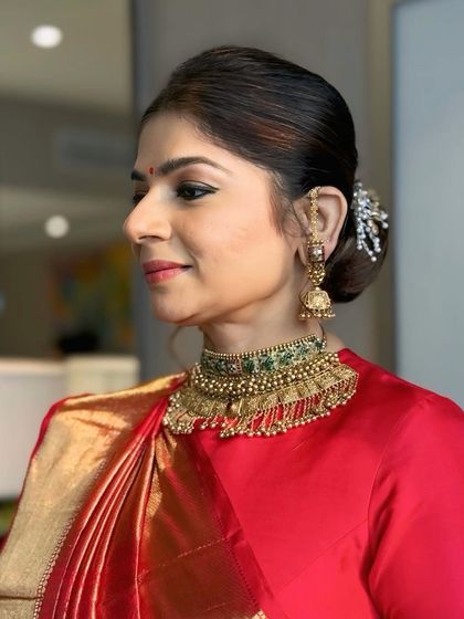 A profile view of a client styled in a classic low bun with a decorative hair accessory. This timeless updo is perfect for a wedding guest or for a bride seeking a sophisticated reception look.