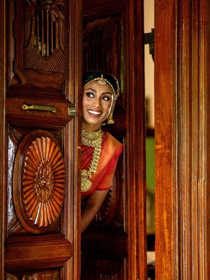 A bride peeks from behind an antique wooden door, her smile full of anticipation.