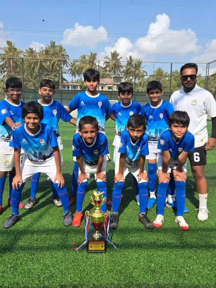 One of our U12 teams in Goa, posing with their coach and their championship trophy on a sunlit pitch.