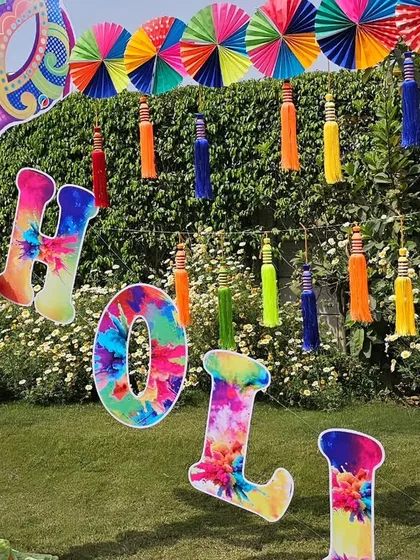 This colorful "Holi" photo arch is one of our most popular designs for the festival of colors. The vibrant paper fans, tassels, and custom lettering create a perfect backdrop for fun pictures at any Holi party or event.