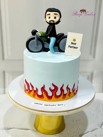 A custom cake for a husband who loves his bike. This design features a fondant figurine on a motorcycle, with fiery details painted along the bottom of the cake.