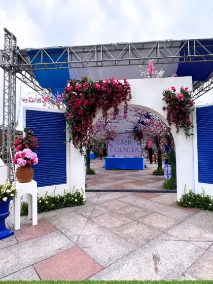A grand entrance designed to feel like stepping into a Santorini postcard. The white and blue structure is adorned with bougainvillea, creating a fresh and festive welcome for a carnival-themed event.