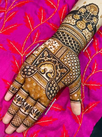 A bold and beautiful back-of-hand design. The central peacock is framed by a square, with a kalash (sacred pot) on the wrist, all set against a dark, filled-in background.