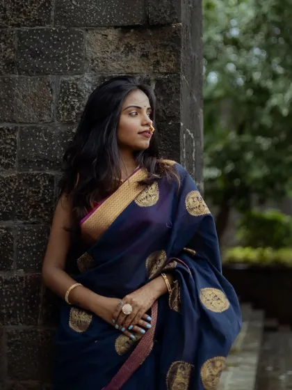 This shot uses the texture of a stone wall as a backdrop to complement the traditional saree. The model's relaxed pose and the natural lighting create a simple yet powerful ethnic portrait.