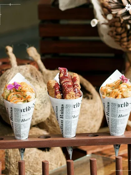 A trio of appetiser cones, featuring different fried snacks with unique sauces. The newspaper print cones add a playful, rustic touch to a modern presentation.